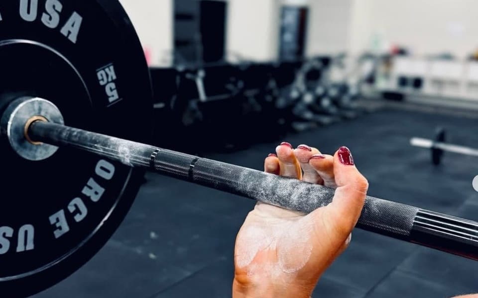 Chalked hands gripping a barbell on the House of Hybrid gym floor.